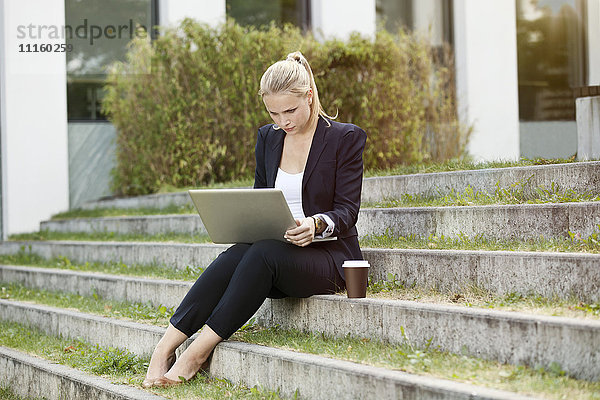 Junge Geschäftsfrauen sitzen auf einer Treppe im Freien mit einem Laptop