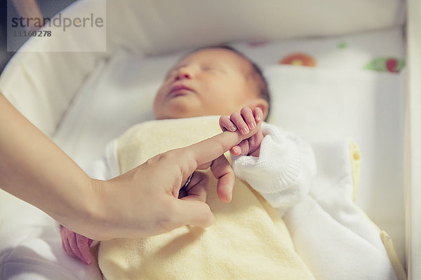 Hand des Neugeborenen mit dem Finger im Krankenhausbett