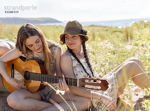 Teenagermädchen spielt Gitarre für ihre Freunde am Strand