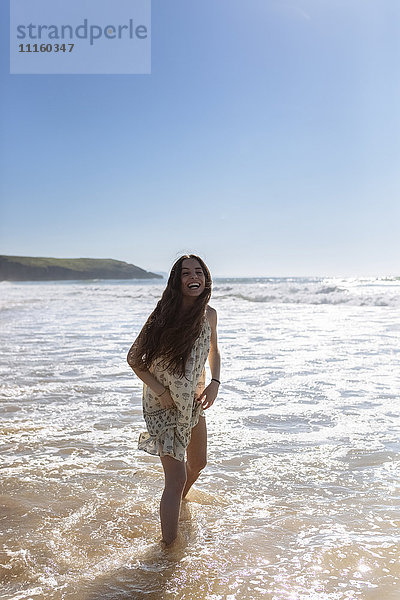 Lachende junge Frau im Wasser am Meer stehend