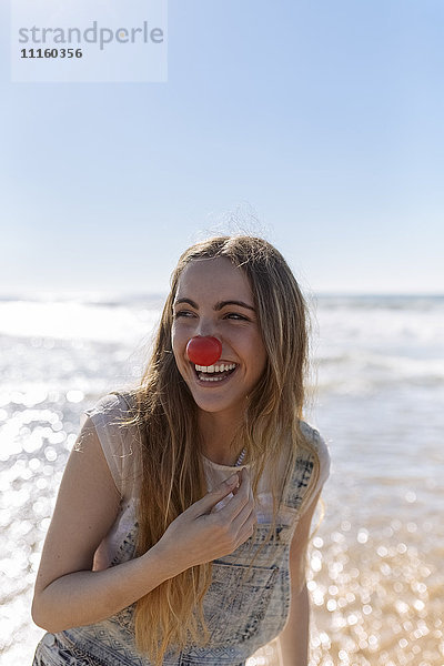 Porträt eines lächelnden Teenagermädchens mit Clownsnase am Meer