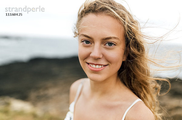 Porträt eines lächelnden blonden Mädchens an der Küste