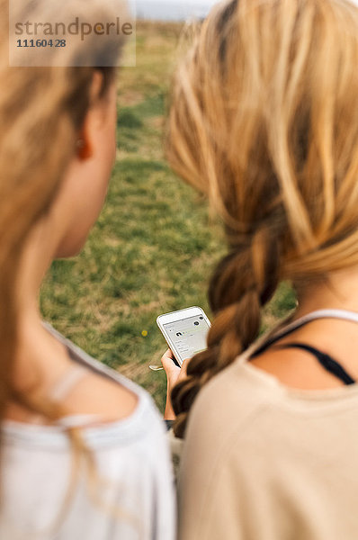 Rückansicht von zwei Teenagermädchen beim Blick auf das Smartphone