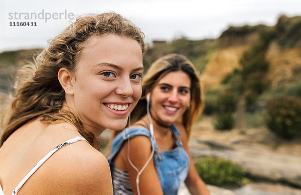 Lächelndes blondes Teenagermädchen beim Musikhören mit ihrer besten Freundin