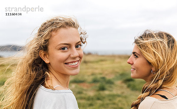 Lächelndes blondes Teenagermädchen und ihre beste Freundin an der Küste