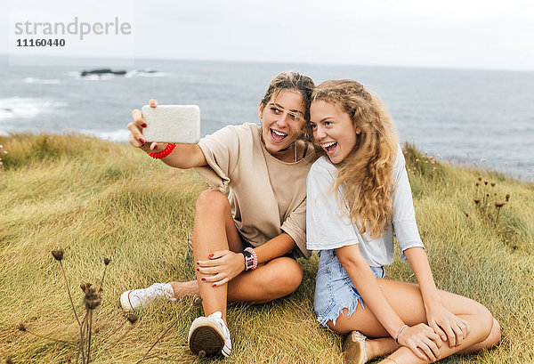 Zwei schreiende Teenager-Mädchen nehmen Selfie an der Küste.