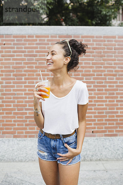Fröhliche junge Frau mit Orangensaft im Freien
