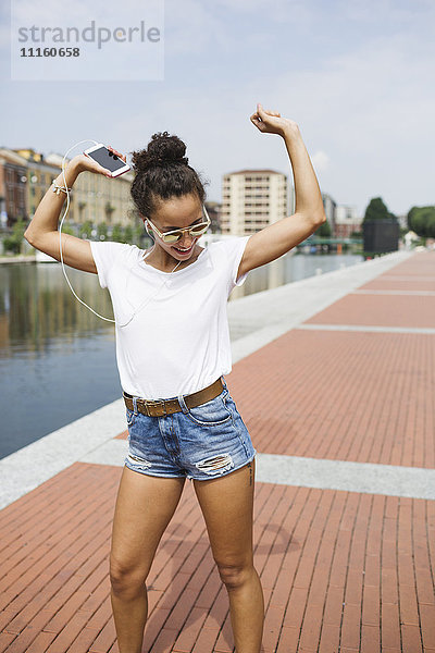 Fröhliche junge Frau beim Musikhören und Tanzen am Flussufer