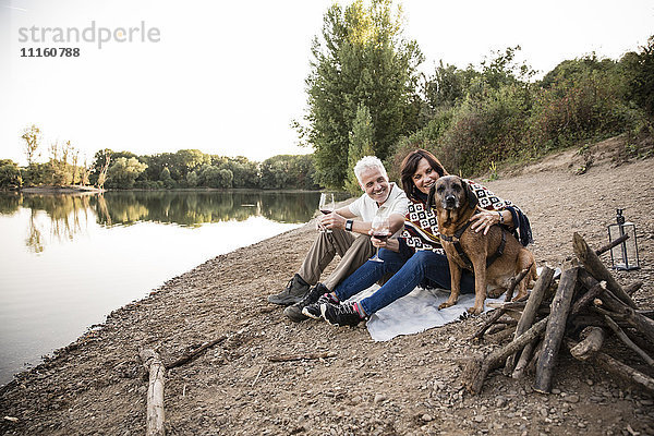 Glückliches Seniorenpaar mit Hund am See am Abend
