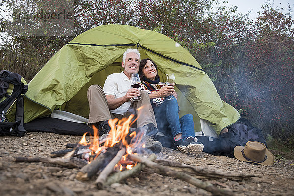 Glückliches Seniorenpaar am Lagerfeuer mit Wein im Zelt