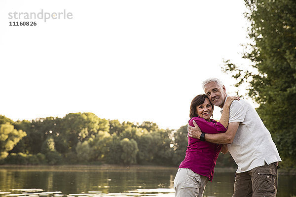 Lächelndes Seniorenpaar umarmt einen See