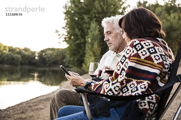 Seniorenpaar mit Wein am See mit Tablette