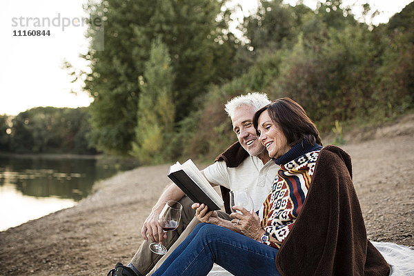Glückliches Seniorenpaar mit Wein und Buch am See