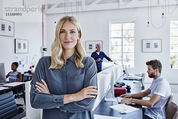 Porträt einer selbstbewussten Geschäftsfrau im Büro mit Mitarbeitern im Hintergrund
