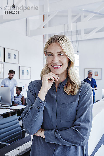 Porträt einer lächelnden Geschäftsfrau im Büro mit Mitarbeitern im Hintergrund