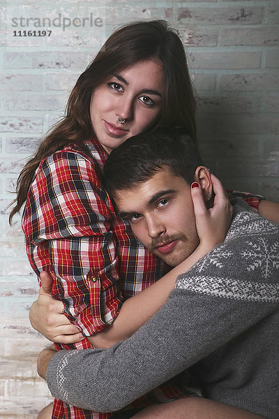 Porträt eines jungen Paares  das sich an der Ziegelwand umarmt.
