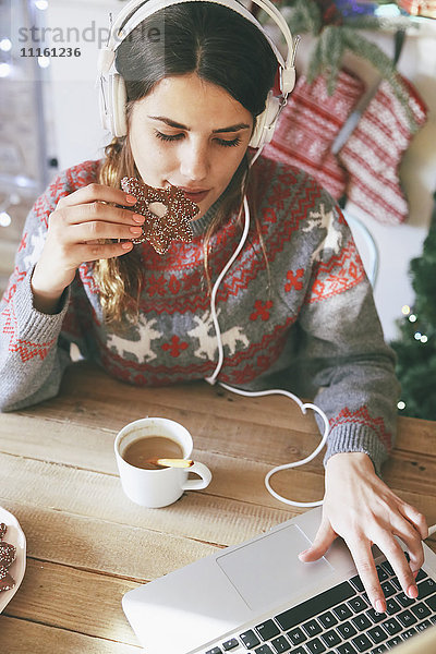 Frau mit Kopfhörer mit Laptop beim Essen Weihnachtsplätzchen