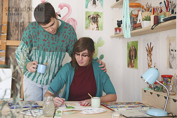 Künstlerin malt in ihrem Atelier  während ihr Freund sie beobachtet.