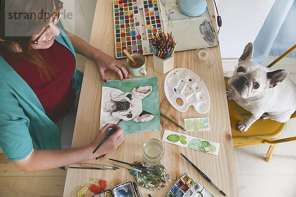 Künstlerin malt ein Aquarell ihrer französischen Bulldogge in ihrem Atelier.