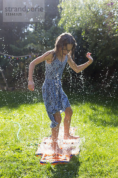 Mädchen hat Spaß mit aufblasbarem Wasserkissen im Garten