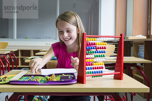 Lächelnde Schülerin sitzt am Schreibtisch in ihrer Klasse