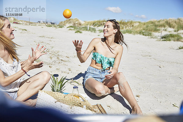 Zwei Freundinnen am Strand werfen eine Orange.