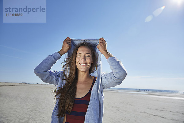 Lächelnde junge Frau mit Kapuze am Strand