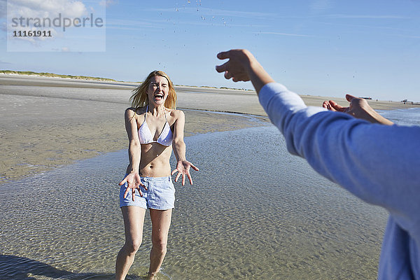 Glückliche junge Frau  die am Strand mit Wasser bespritzt wird.