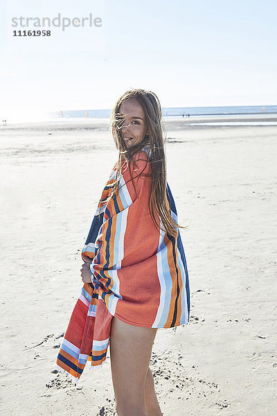 Lächelnde junge Frau in eine Decke am Strand gewickelt