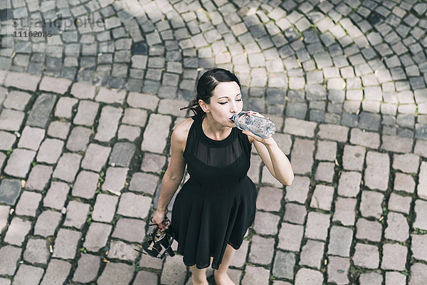 Junge Frau auf Kopfsteinpflaster stehend Trinkwasser aus der Flasche