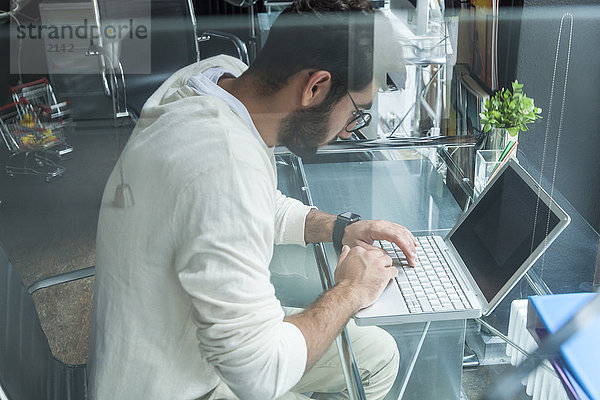 Junger Mann arbeitet mit Laptop am Schreibtisch in einem modernen Büro