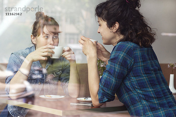 Zwei Frauen sitzen hinter der Fensterscheibe eines Cafés und trinken Kaffee.