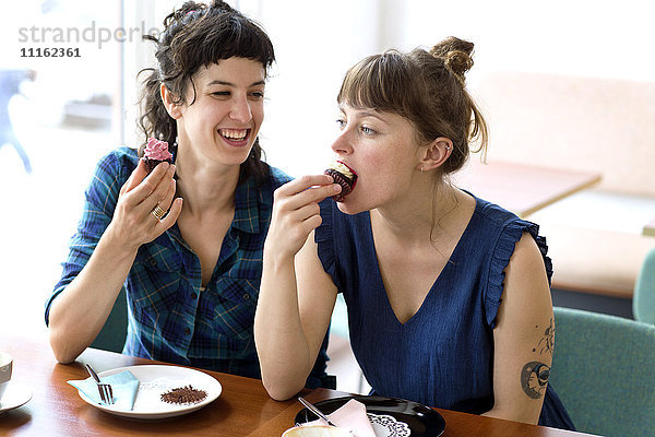 Zwei Freunde sitzen nebeneinander in einem Café und essen Tassenkuchen.