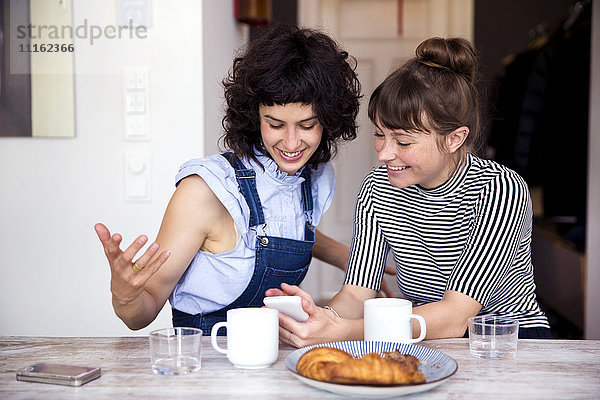Zwei Frauen am Frühstückstisch beim gemeinsamen Blick auf das Smartphone