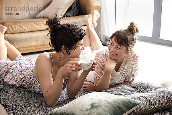 Zwei sprechende Freunde liegen auf einer Decke auf dem Boden des Wohnzimmers.