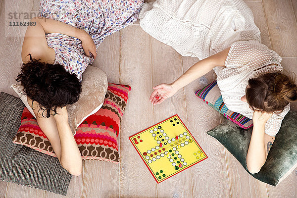Draufsicht von zwei besten Freunden  die zu Hause auf dem Boden liegen und Ludo spielen.