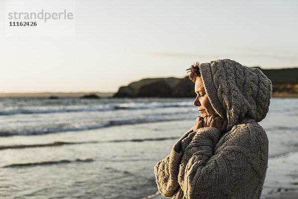 Frankreich  Halbinsel Crozon  Frau mit Strickjacke am Strand bei Sonnenuntergang