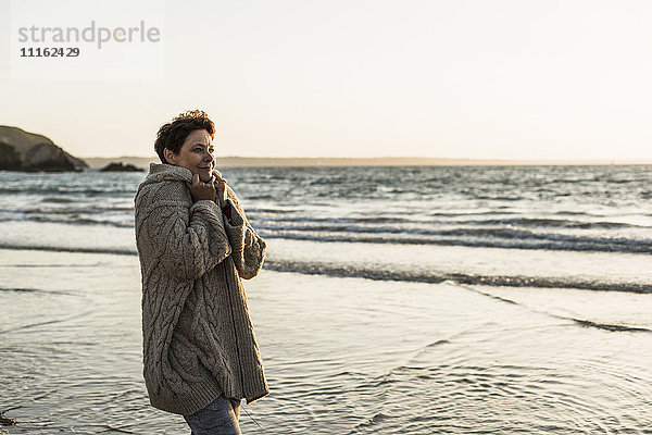 Frankreich  Halbinsel Crozon  Frau mit Strickjacke am Strand bei Sonnenuntergang