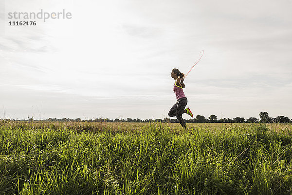Junge Frau beim Seilhüpfen in ländlicher Landschaft