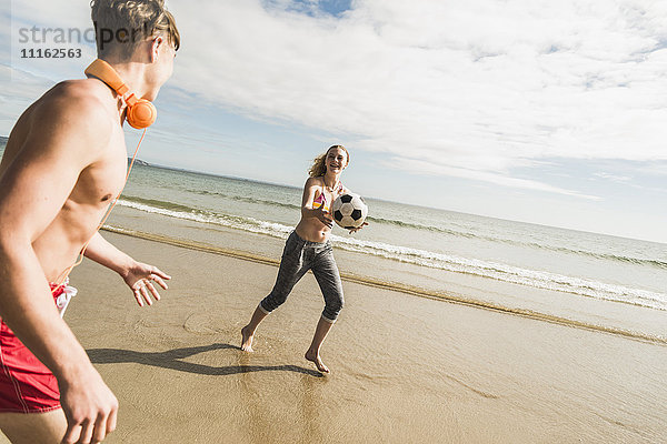 Teenager-Mädchen und junger Mann spielen mit einem Ball am Strand