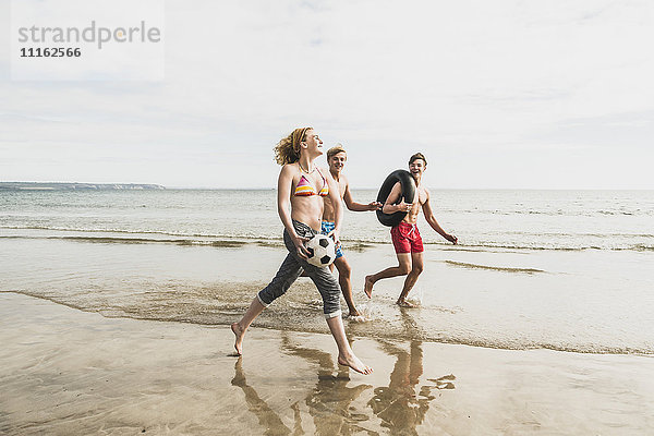 Freunde  die mit Ball und Reifen am Strand spazieren gehen.