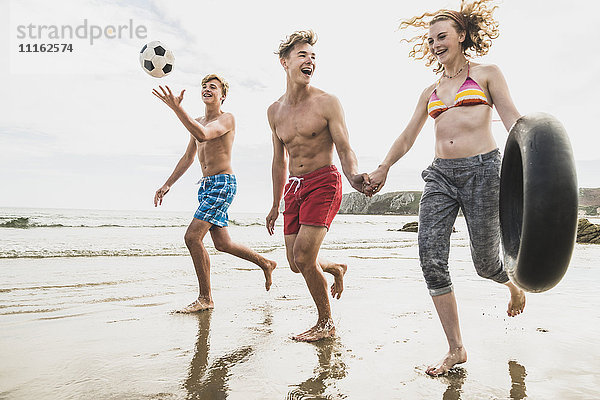 Freunde beim Laufen mit Ball und Reifen am Strand