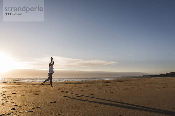 Frankreich  Bretagne  Halbinsel Crozon  Frau beim Springen am Strand bei Sonnenuntergang