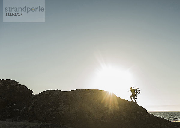 Frankreich  Crozon-Halbinsel  Mountainbiker mit dem Fahrrad bei Sonnenuntergang