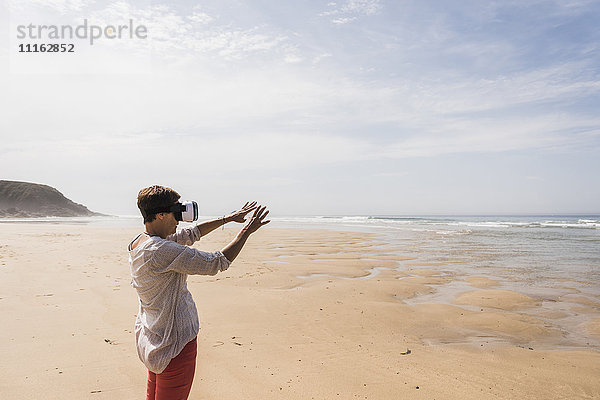 Reife Frau am Strand stehend mit VR-Brille