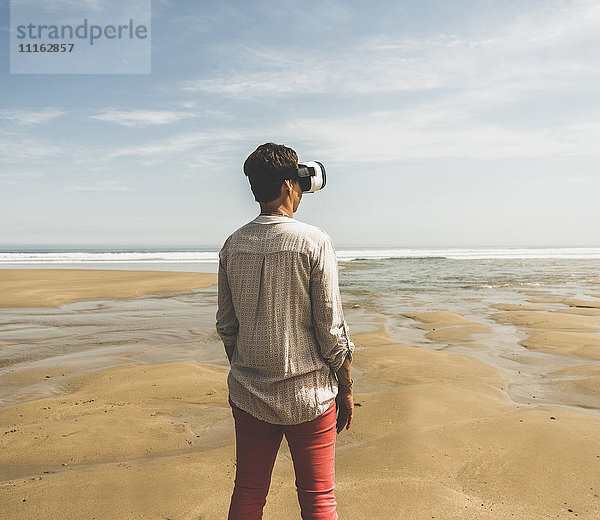 Reife Frau am Strand stehend mit VR-Brille