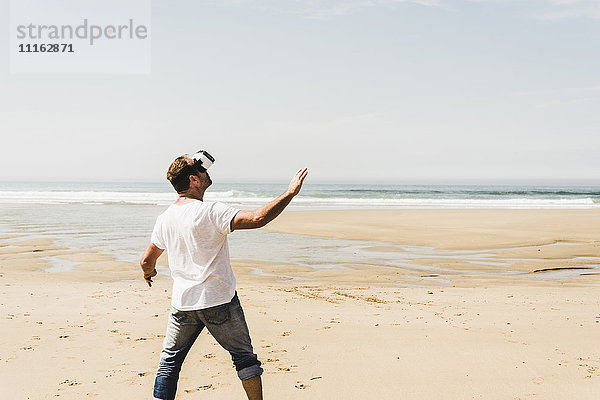 Erwachsener Mann am Strand stehend mit VR-Brille