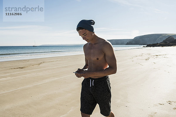 Frankreich  Halbinsel Crozon  junger Mann mit Handy am Strand unterwegs