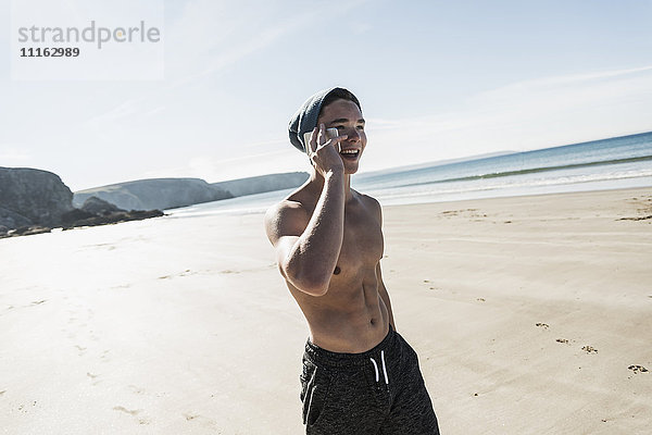 Frankreich  Halbinsel Crozon  glücklicher junger Mann auf dem Handy am Strand