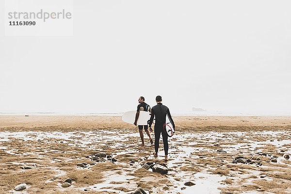 Frankreich  Bretagne  Halbinsel Crozon  Paar mit Surfbrettern am Strand spazieren gehen
